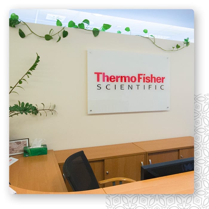 Szklany szyld firmowy z nadrukiem logo Thermo Fisher Scientific zamontowany na dystansach w recepcji.